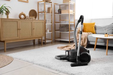 Elektrik süpürgesi, çekmeceler ve raf üniteleriyle aydınlık oturma odasının içinde.