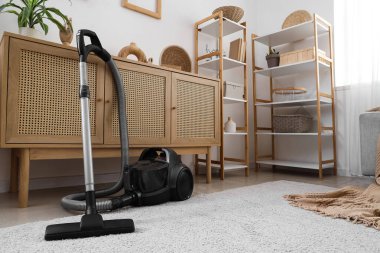 Elektrik süpürgesi, klozet ve raf üniteleriyle aydınlık oturma odasının içinde.