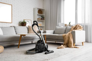 Oturma odasının içinde elektrikli süpürge, kanepe ve masa var.