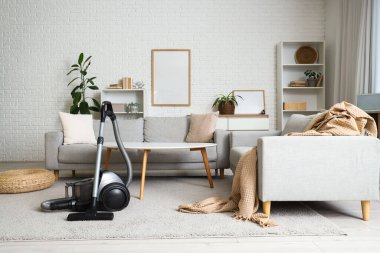 Oturma odasının içinde elektrikli süpürge, kanepe ve masa var.