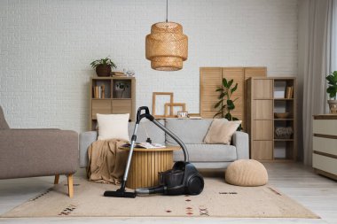 Oturma odasında elektrikli süpürge, masa ve kanepe var.