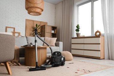 Oturma odasında elektrikli süpürge, masa ve kanepe var.