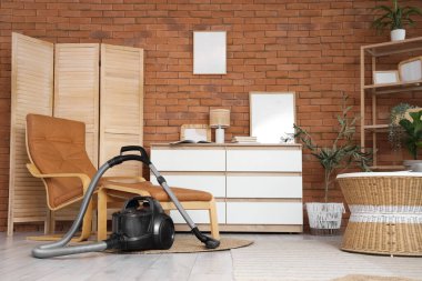 Oturma odasının içinde elektrikli süpürge, koltuk ve çekmeceler var.