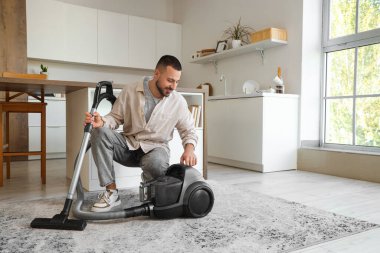 Mutfakta elektrikli süpürgesi olan genç bir adam.