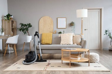 Oturma odasının içinde elektrikli süpürge, kanepe ve masa var.