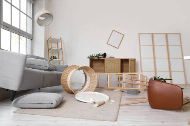 Kanepeli dağınık bir oturma odası, ters çevrilmiş masa ve deprem sonrası raf üniteleri.