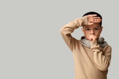 Hafif arka planda öksüren küçük Asyalı çocuk.