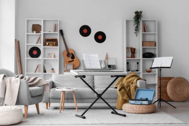 Aydınlık oturma odasının içinde sentezleyici, koltuk ve koltuk var.