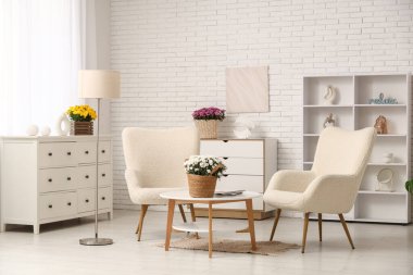 Oturma odasının içinde koltuklar, masa ve kasımpatı çiçekleri