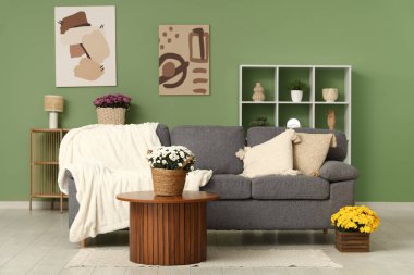 Oturma odasında kanepe, masa ve kasımpatı çiçekleri var.