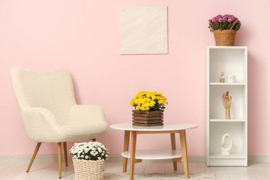 Oturma odası, koltuk, raf ünitesi ve kasımpatı çiçekleri.