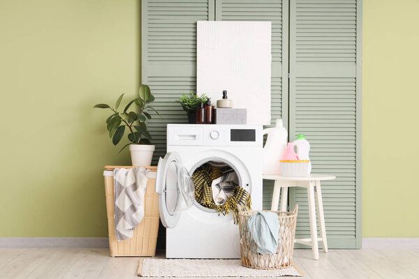Интерьер прачечной с зеленым складным экраном, стиральной машиной и корзиной