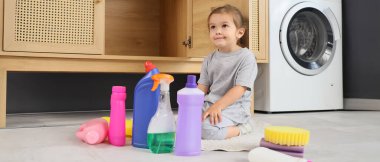 Little girl with detergents in laundry room. Child in danger clipart