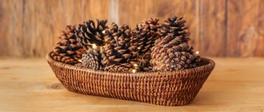 Çam kozalaklı hasır kase ve ahşap arka planda parlayan Noel ışıkları
