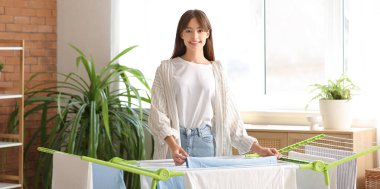 Çamaşır odasında temiz giysileri kurutucuya asan güzel bir genç kadın.