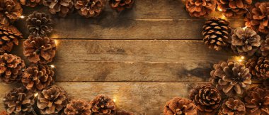 Çam kozalaklarından yapılmış çerçeve ve ahşap arka planda Noel ışıkları, üst manzara