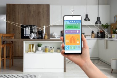 Akıllı ev otomasyonunun açık uygulamasıyla el ele tutuşan cep telefonu mutfakta ekranda