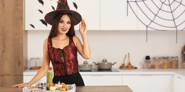 Cadılar Bayramı için dekore edilmiş mutfakta cadı gibi giyinmiş güzel bir Asyalı kadın. 