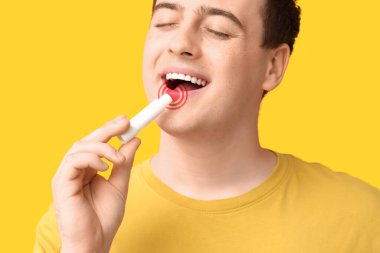 Genç adam sarı arka plana dudak kremi sürüyor.