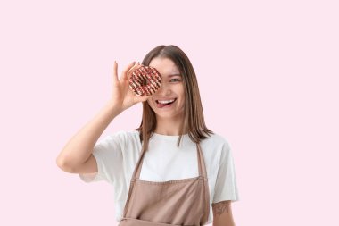 Pembe arka planda donutu olan önlüklü güzel bir kadın.