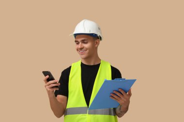 Genç erkek mühendis, arkaplanda not panosu ve cep telefonu var.