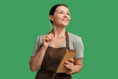 Yeşil arka planda defter ve kalemle güzel bir garson kız.