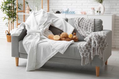 Beyaz bornoz ve oturma odasındaki kanepede farklı banyo malzemeleri.