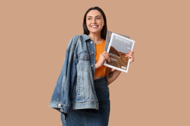 Bej arka planda dergileri olan şık kot elbiseli güzel, genç ve mutlu bir kadın.