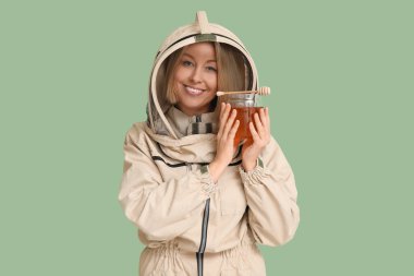 Female beekeeper with jar of sweet honey and dipper on green background clipart