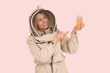 Female beekeeper pointing at jar of sweet honey on pink background clipart