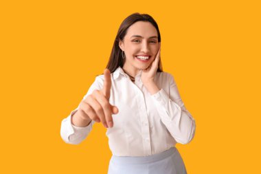 Gülümseyen genç kadın sarı arka plandaki bir şeyi işaret ediyor.