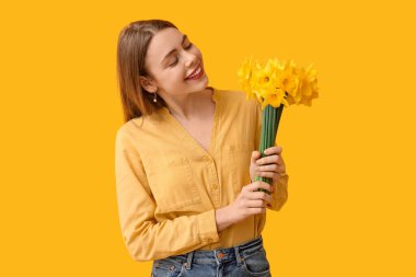 Sarı arka planda bir buket güzel nergis çiçeğiyle mutlu genç bir kadın.