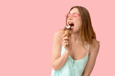 Young woman biting ice cream in waffle cone on pink background clipart