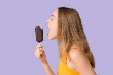 Young woman biting chocolate covered ice cream on lilac background clipart