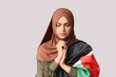 Filistin bayrağı taşıyan genç Müslüman kadın gri arka planda dua ediyor. Üzüntü konsepti