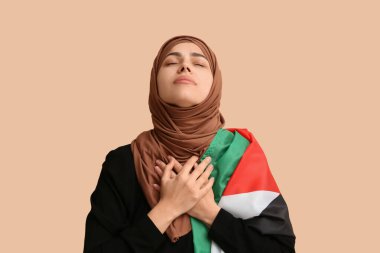 Filistin bayrağı taşıyan genç Müslüman kadın bej arka planda dua ediyor. Üzüntü konsepti