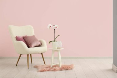 Yastıklı beyaz koltuk, orkideli kahve masası ve pembe duvarlı yumuşak halı.