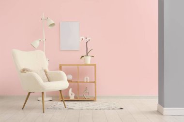Pembe duvarın yanında beyaz koltuk, lamba ve raf ünitesi