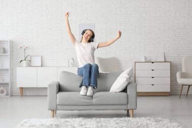 Kulaklıklı genç ve güzel bir kadın oturma odasındaki kanepede müzik dinliyor.