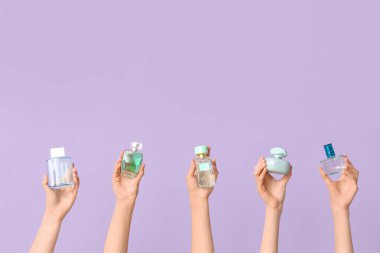 Leylak arka planında bir sürü parfüm şişesi olan kadın elleri.