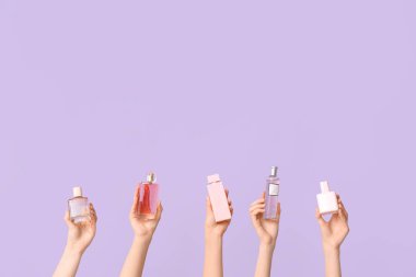 Leylak arka planında farklı parfüm şişeleri olan kadın elleri.