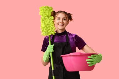 Pembe arka planda paspas ve leğen taşıyan genç bir kadın.