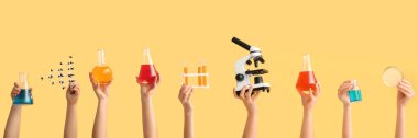 Laboratuvar cam, mikroskop, molekül modeli ve sarı arka planda Petri kabı olan birçok el.