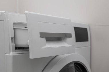 Işık duvarının yanında açık deterjan çekmecesi olan modern çamaşır makinesi.