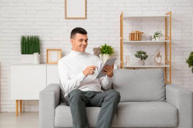 Evde online randevuda tablet bilgisayar kullanan yakışıklı genç adam.
