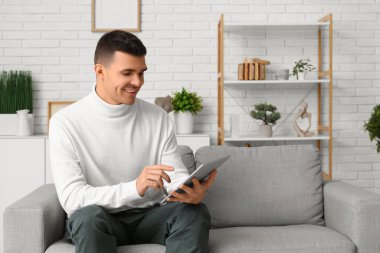 Evde online randevuda tablet bilgisayar kullanan yakışıklı genç adam.