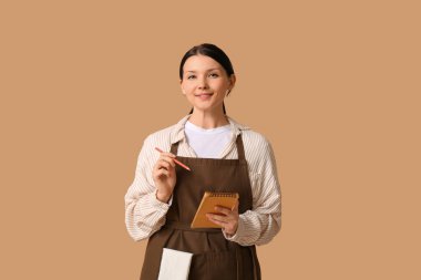 Kahverengi arka planda defter ve kalemle güzel bir garson kız.