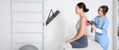 Fizyoterapist, rehabilitasyon merkezinde genç bir kadının omurgasına perküsyon masajı yapıyor.