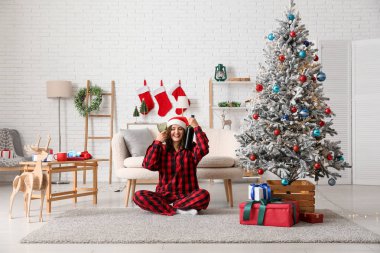 Noel Baba şapkası ve bir şişe şarapla Noel için dekore edilmiş bir odada oturan güzel genç kadın.
