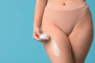 Mavi arka planda anti-selülit kremi kavanozu olan güzel genç bir kadın.